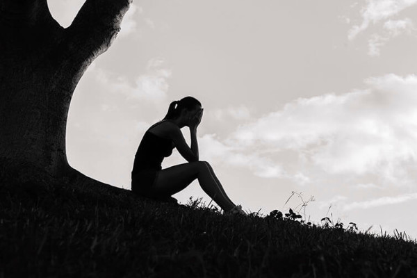 Woman sitting under tree with head in hands